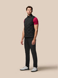 Male model wearing black Pinnacle Gilet over a magenta shirt standing against a beige background.