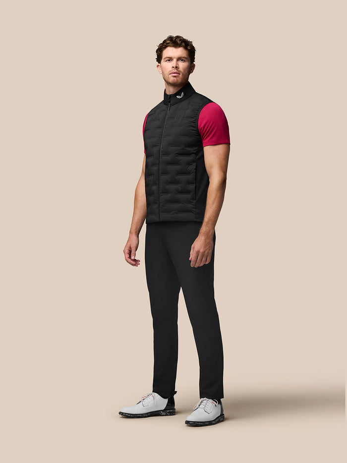 Male model wearing black Pinnacle Gilet over a magenta shirt standing against a beige background.