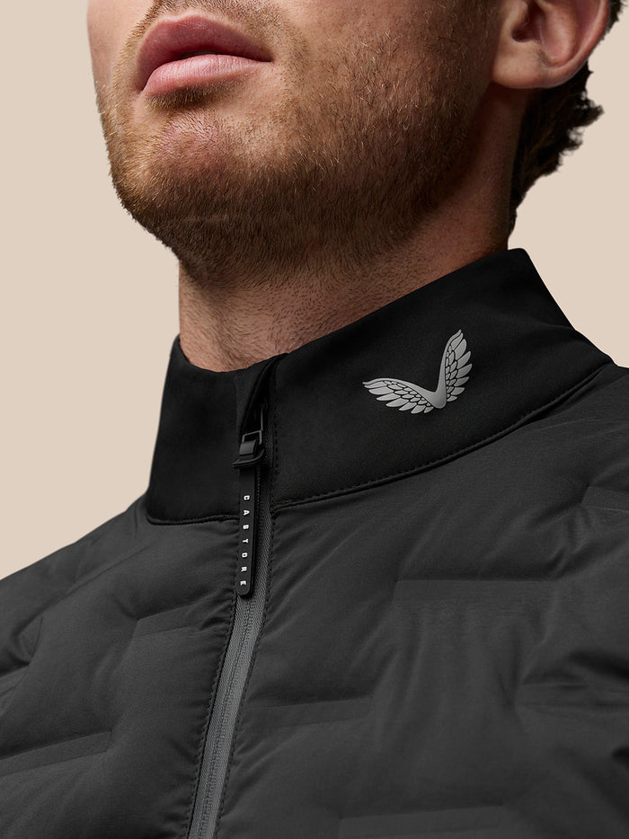 Close-up of black stand collar golf gilet with a silver wing logo near the zipper.
