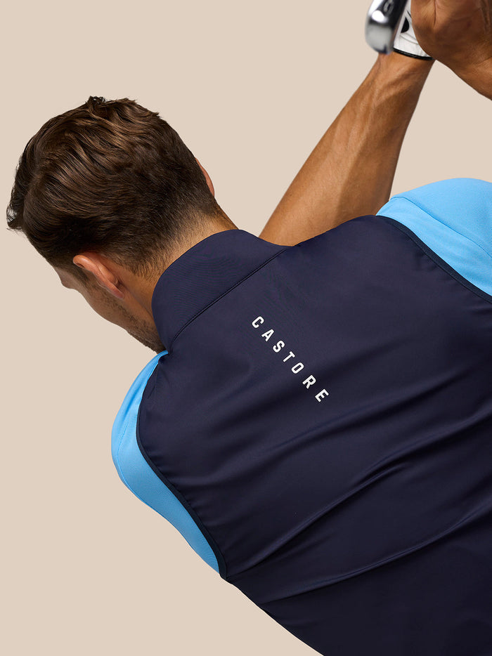 Back view of male model wearing navy Pinnacle Gilet over a blue top with CASTORE branding on the back.