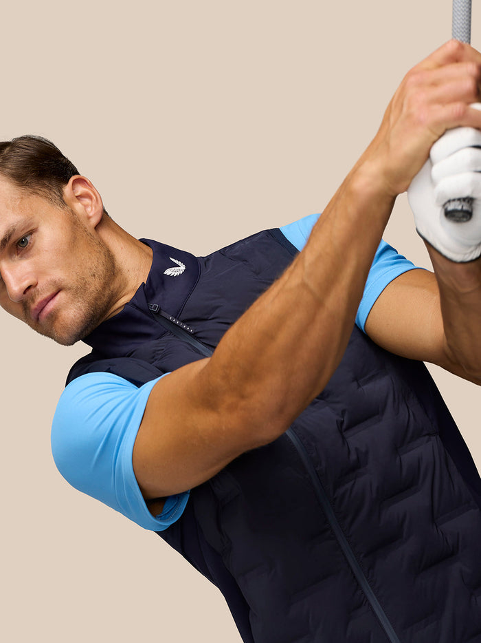 Male golfer wearing navy Pinnacle Gilet with light blue sleeves and holding a golf club overhead