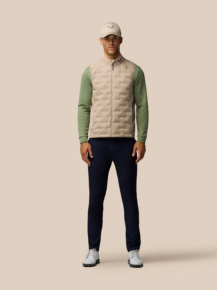 Male model wearing Golf Pinnacle Mushroom gilet with beige front and green sleeves, cap, and navy pants