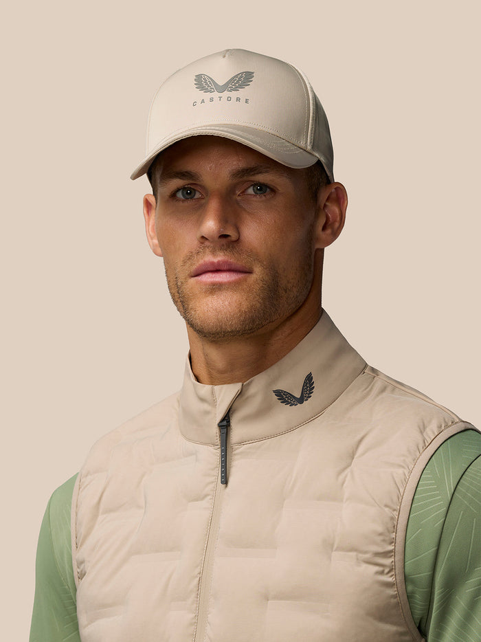 Model wearing beige Pinnacle lightweight hybrid gilet over sage-green top with cap.