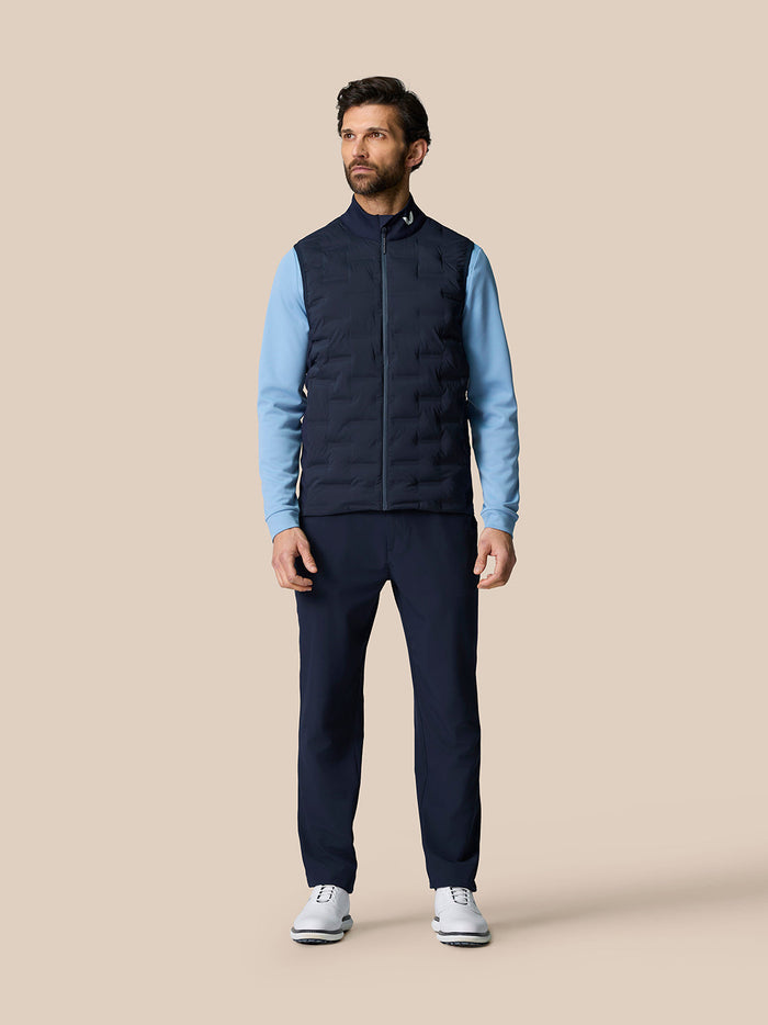 Male model wearing midnight navy golf gilet with quilted panels, stand collar and front zip over a light blue top