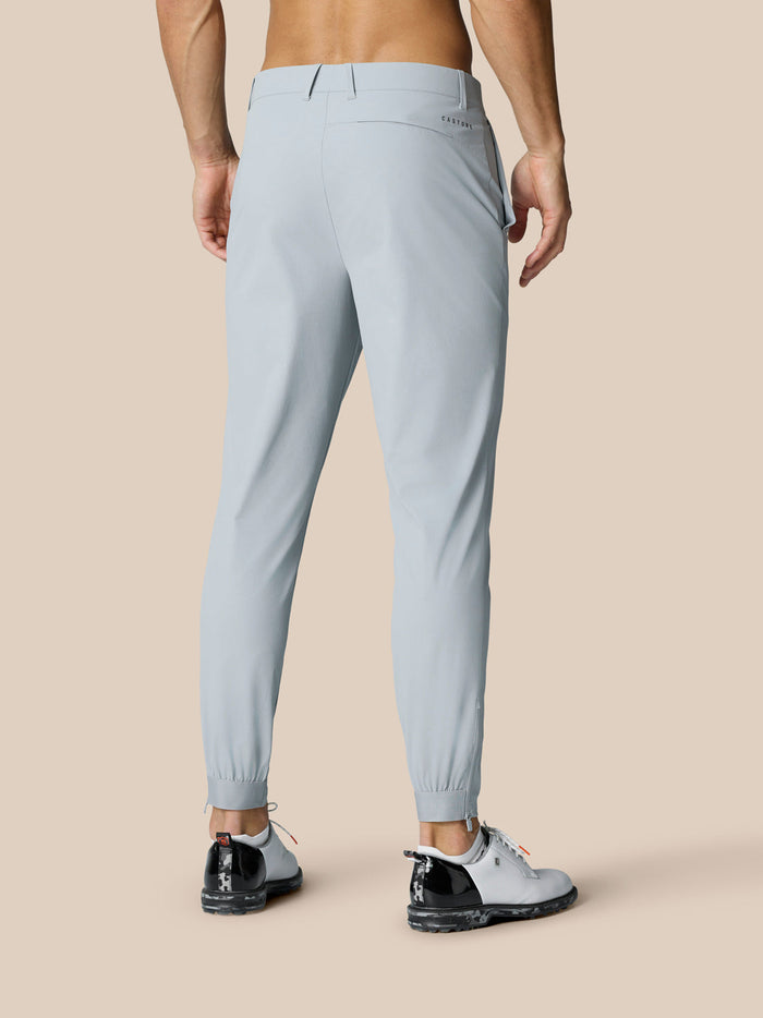 Back view of a male model wearing light grey Castore Golf Pinnacle 34 trousers with belt loops and cuffed ankles.
