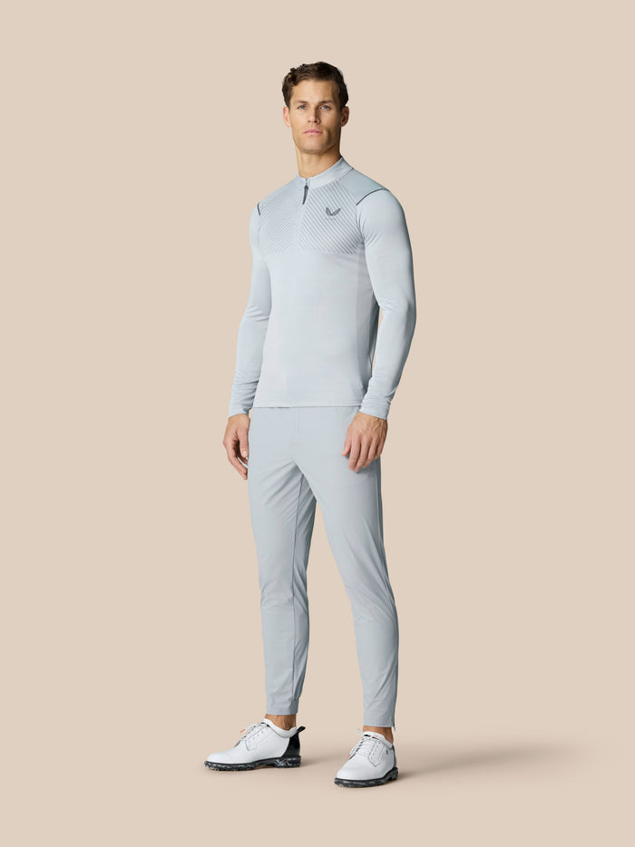 Male model wearing light grey golf top and Pinnacle 32 trousers in mid grey against a neutral backdrop