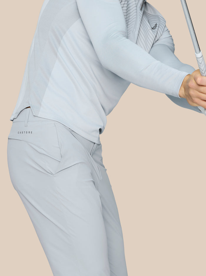 Close up of a golfer's midsection in light grey outfit gripping a club, Castore logo visible on the trousers