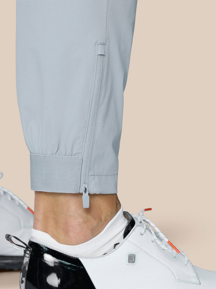 Close-up of light grey golf trousers leg with a lower leg zipper, elastic cuff, and strap detail