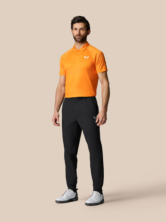 Male model wearing Golf Pinnacle 32 inch black trousers with an orange polo shirt