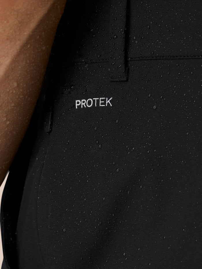 Close-up of black golf trousers fabric with water droplets and PROTEK branding.