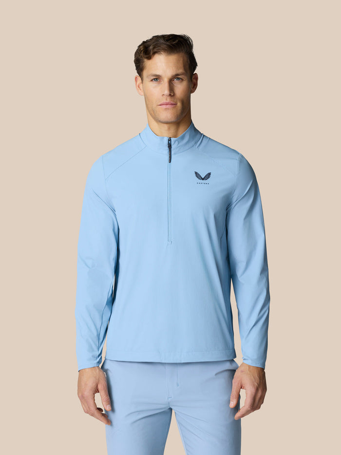 Man wearing sky blue Golf Flex Jacket with high funnel neckline front half zip and Castore graphic.