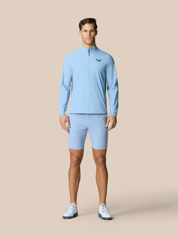Full body shot of a man in sky blue Castore Golf Flex Half Zip Jacket with half zip front and matching shorts.