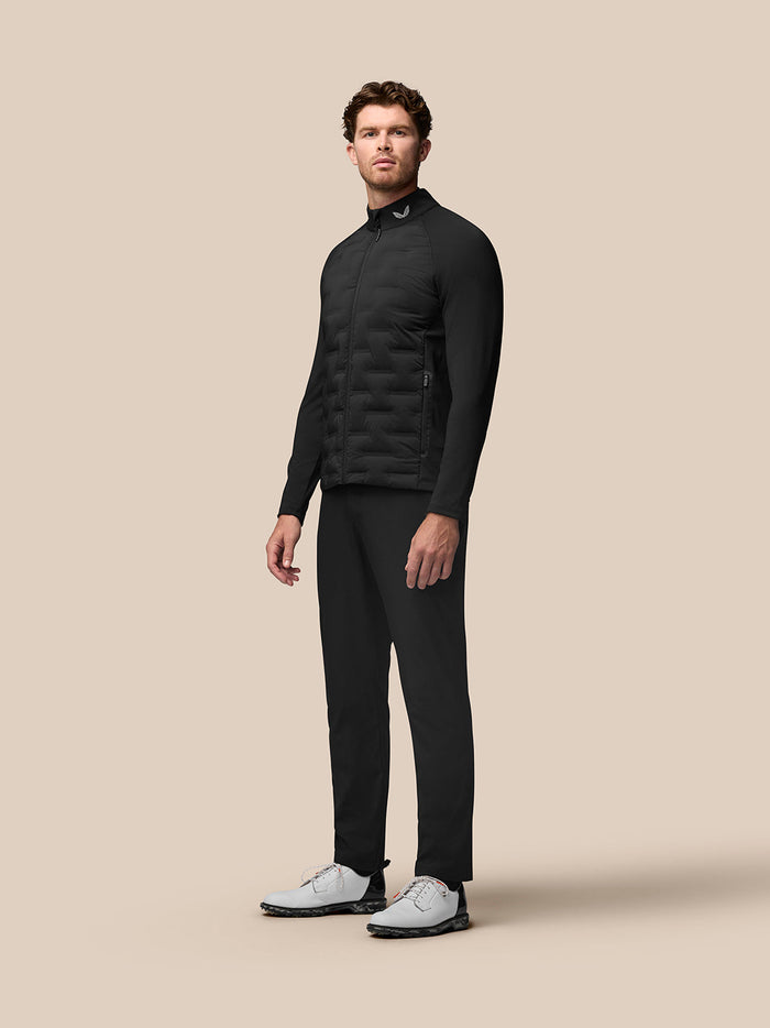 Side profile of a male model in the black Golf Pinnacle Jacket with quilted front panels and stand collar, paired with dark pants and white shoes