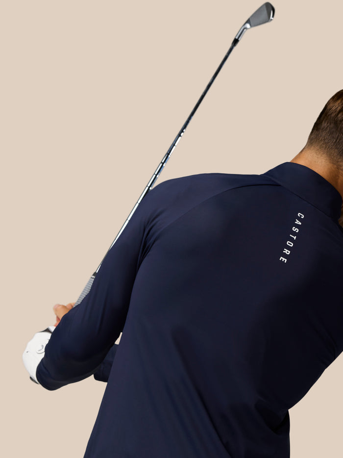 Model wearing Golf Pinnacle Jacket in midnight navy with a golf club resting over the shoulder against a beige background
