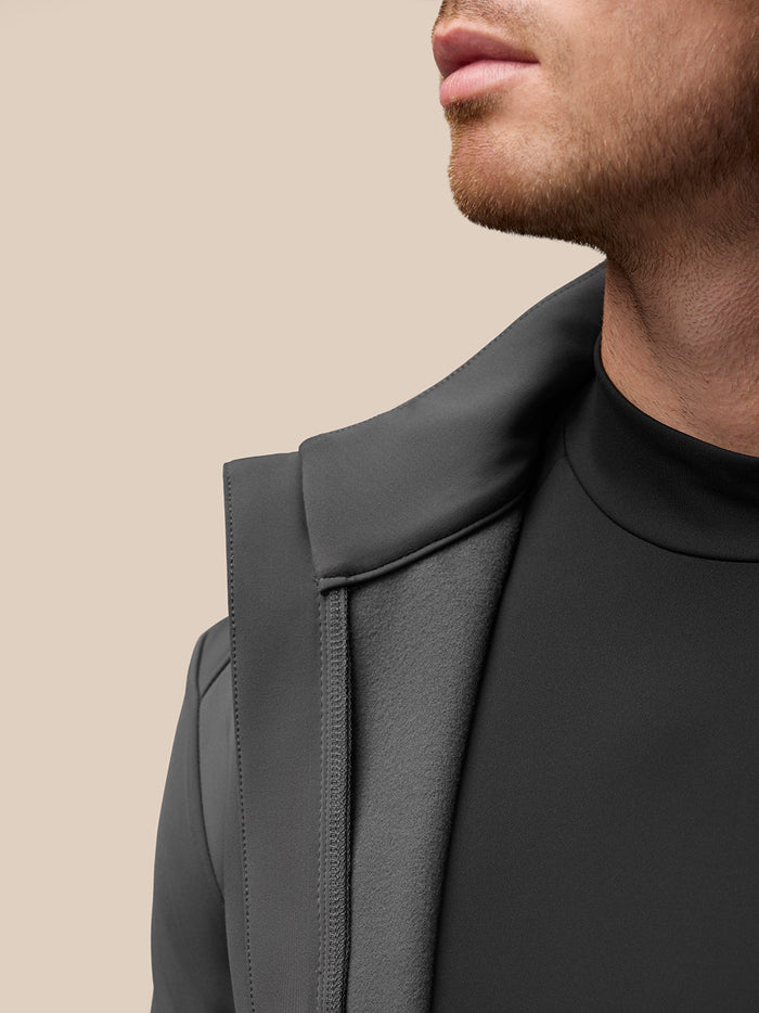 Profile view of a man wearing a dark Castore jacket with a stand collar in a neutral backdrop