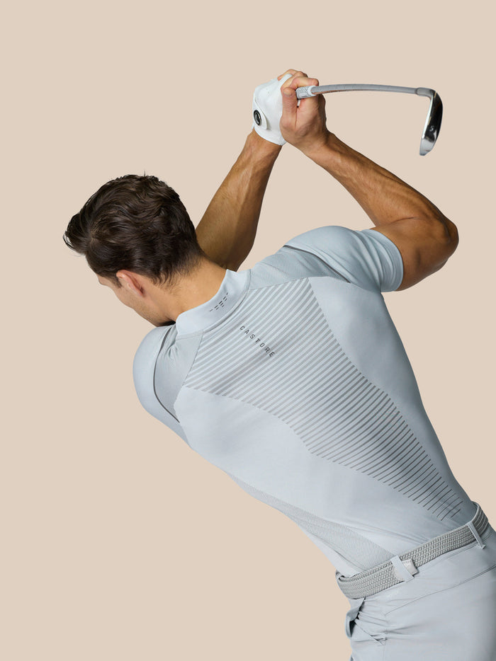 Rear three-quarter view of a man in a light grey polo with diagonal back ventilation stripes