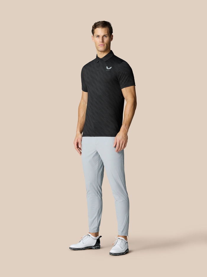 Male model in black Club Graphic Polo with a small left chest logo and light grey pants.