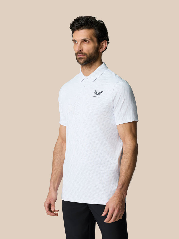 Man facing forward in a white polo with Castore crest on the left chest, standing against a beige background.