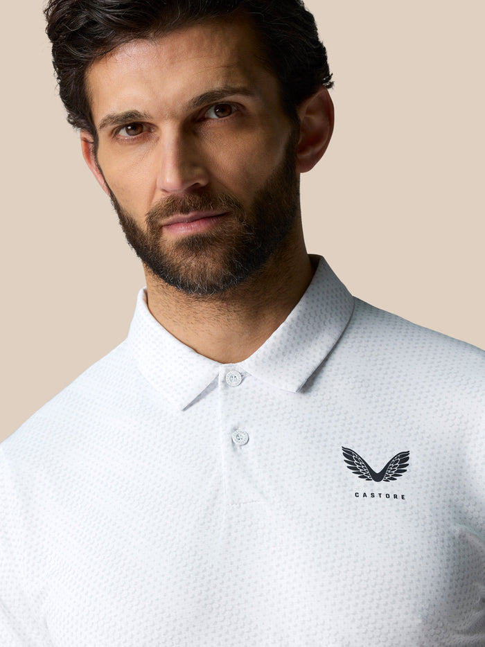 Close up of a man wearing a white Club Graphic Polo with golf ball print, pointed collar and CASTORE logo on the left chest.
