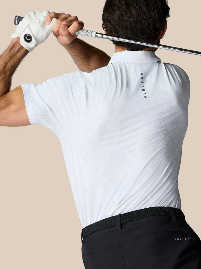 Back view of a man in a white textured polo holding a golf club across his shoulders, Castore branding along the upper back.