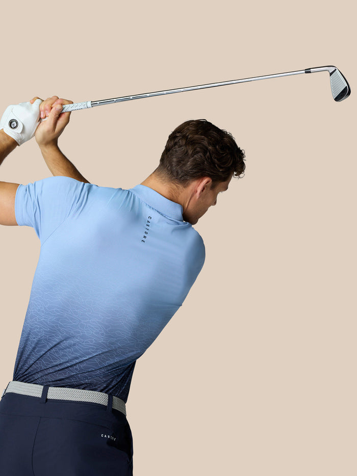 Back view of golfer in Sky Blue Club Graphic Polo showing gradient pattern and Castore branding along upper back.