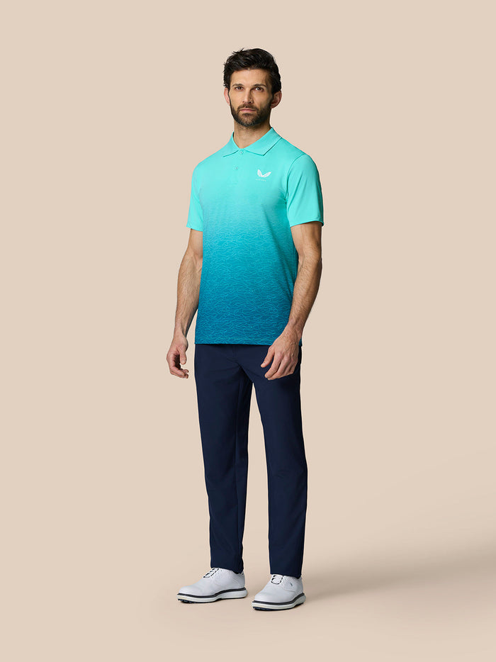 Full-body shot of a man in a light aqua Club Graphic Polo with a gradient pattern, paired with navy trousers and white shoes.