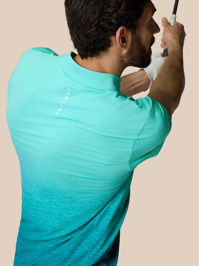 Back view of a man in light aqua Club Graphic Polo with ombre pattern and Castore branding on back during a golf swing.
