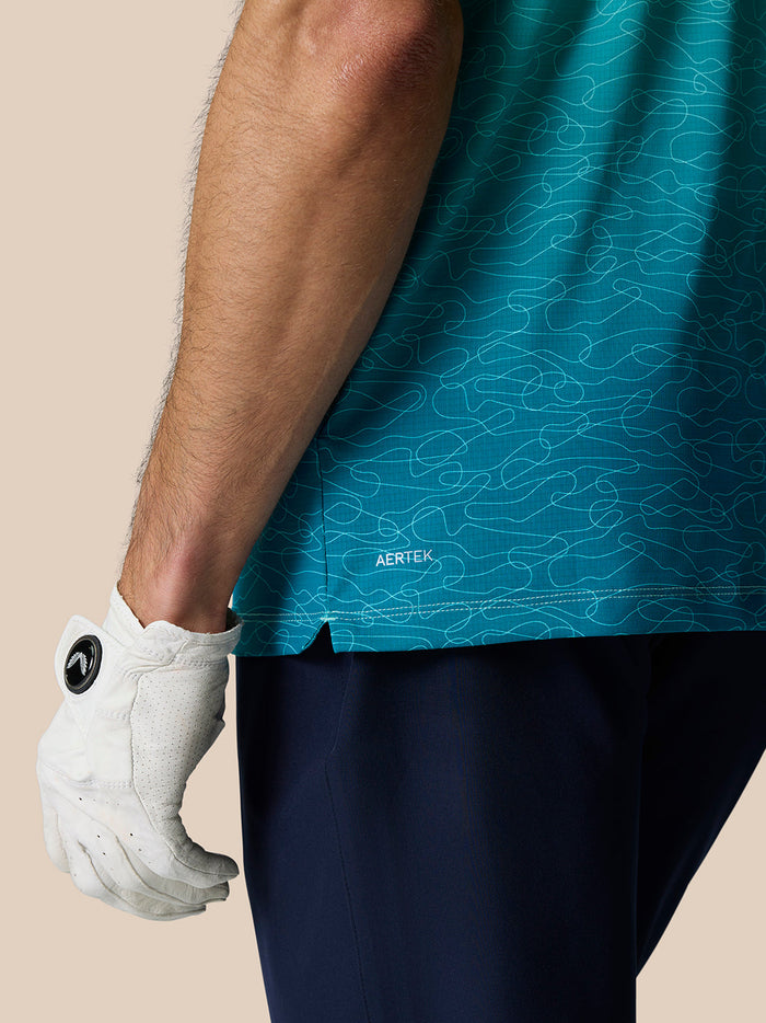 Close-up of a teal Club Graphic Polo sleeve and hem with an AERTEK label and a white golf glove.