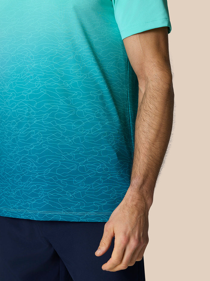 Full-body view of a man wearing a light aqua Club Graphic Polo with an ombre print and navy trousers.