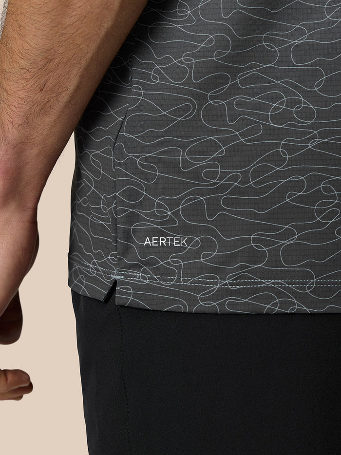 Close-up of the polo lower back with AERTEK branding and a fine abstract swirling pattern on dark grey fabric.
