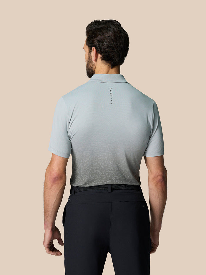 Back view of a man wearing a light grey Club Graphic Polo with vertical Castore branding on the upper back and a subtle ombre on the lower hem.