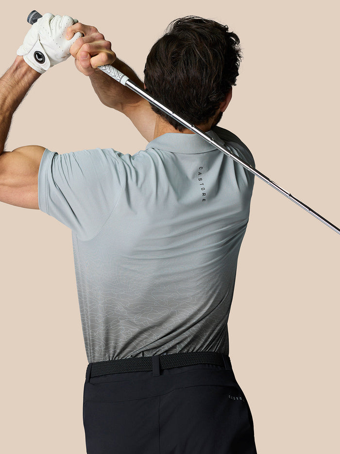 Golfer wearing light grey Club Graphic Polo while swinging a golf club showing an ombre print and Castore branding.