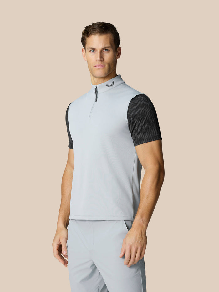 Male model wearing a light grey sleeveless golf gilet with a high neck and half zip, Castore logo at the neckline.