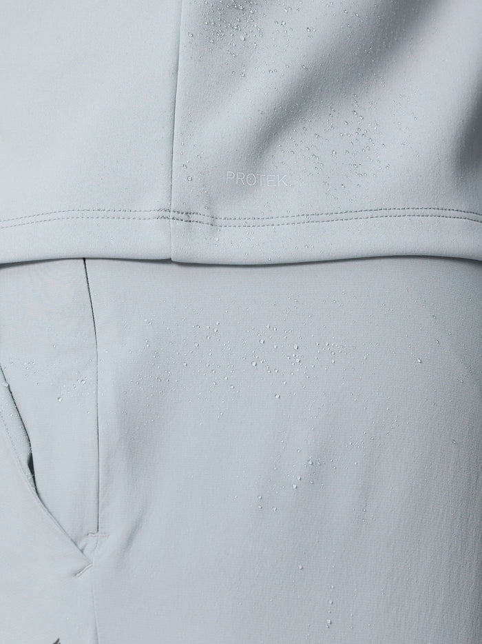 Close-up of light grey Castore golf gilet fabric with water droplets and ProTek branding
