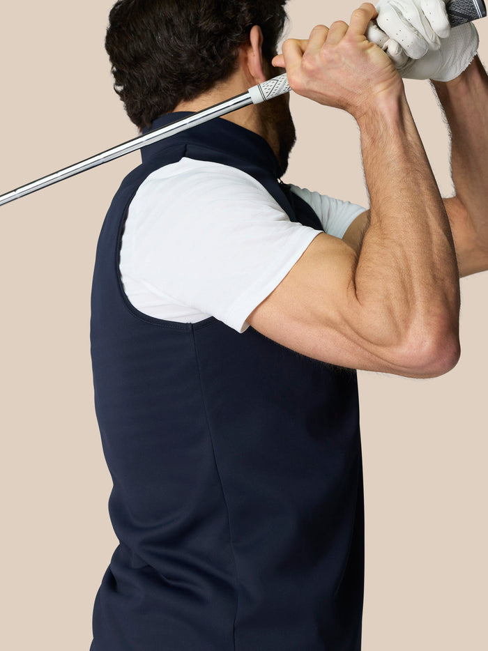 Male model wearing navy Club 1/2 Zip Gilet over a white tee, holding a golf club.