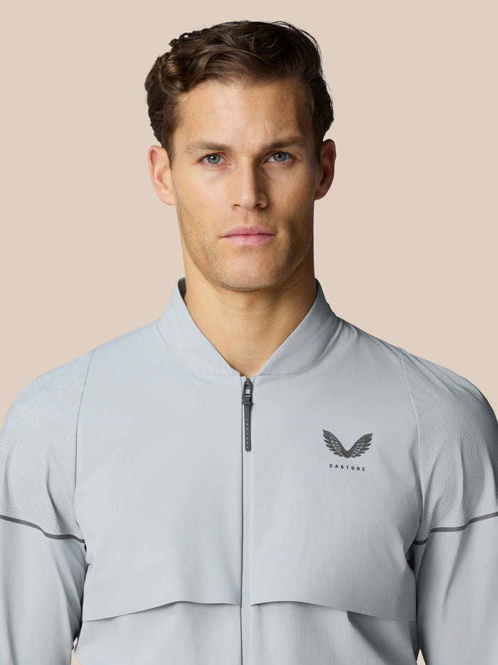 Male model wearing mid grey Golf Pinnacle LVS Woven Jacket with zip front and chest logo, close-up product shot