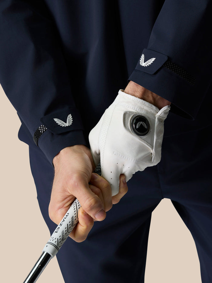 Midnight Navy Golf Pinnacle LVS Woven Jacket worn by a golfer gripping a club, cuff wing logo visible.