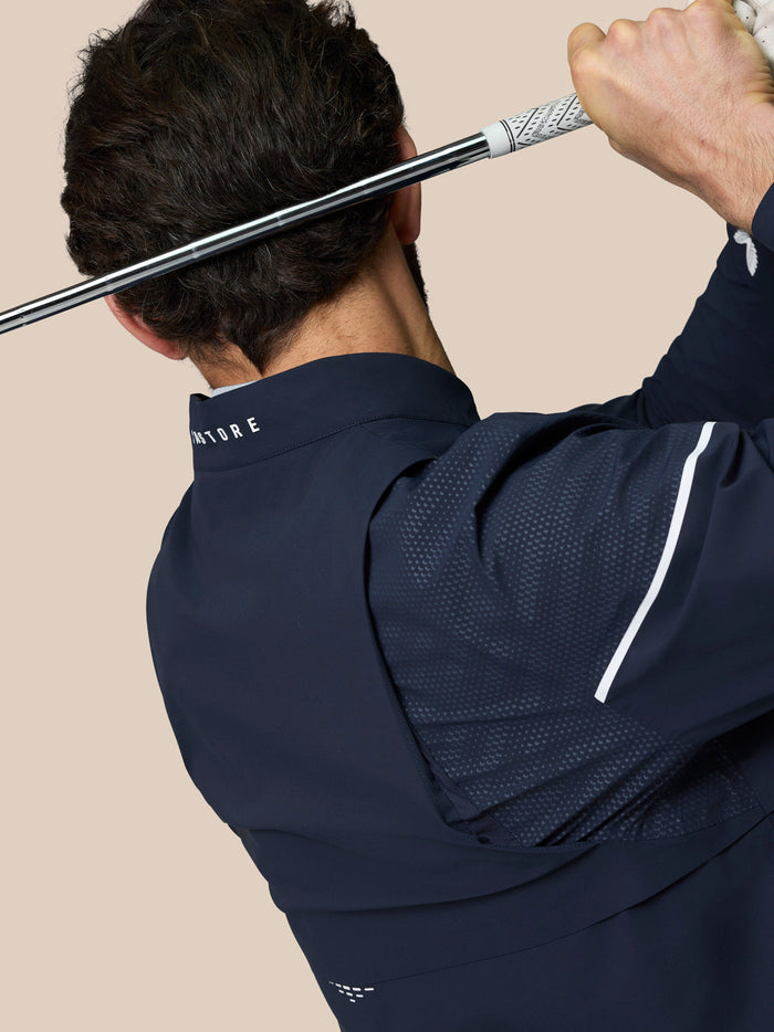 Rear view of a golfer in Midnight Navy LVS Woven Jacket holding a golf club overhead with vented back and mesh panels