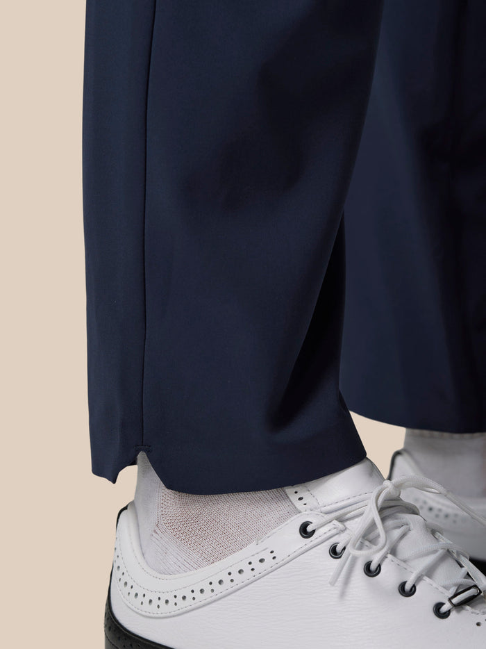 Close-up of navy golf winter trouser leg with vented hem over a white lace-up golf shoe.