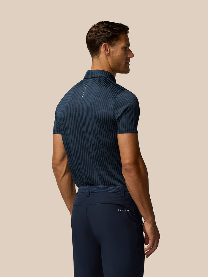 Back view of a man wearing a navy striped golf polo with vertical stripes and the Castore logo along the back.