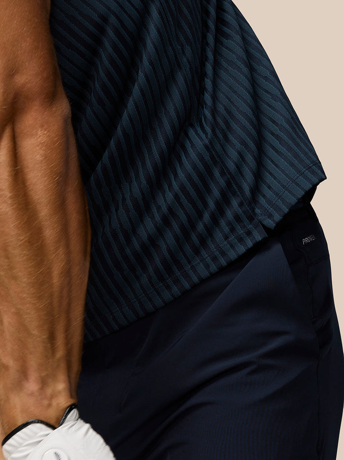 Close-up detail of the navy striped knit polo fabric showing the textured stripes with a belt and navy pants.