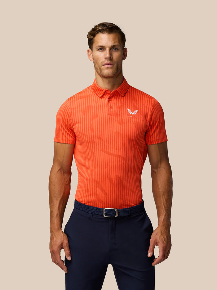 Front view of a man in a bright orange striped Golf Pinnacle Glow Polo with Castore logo on the chest.