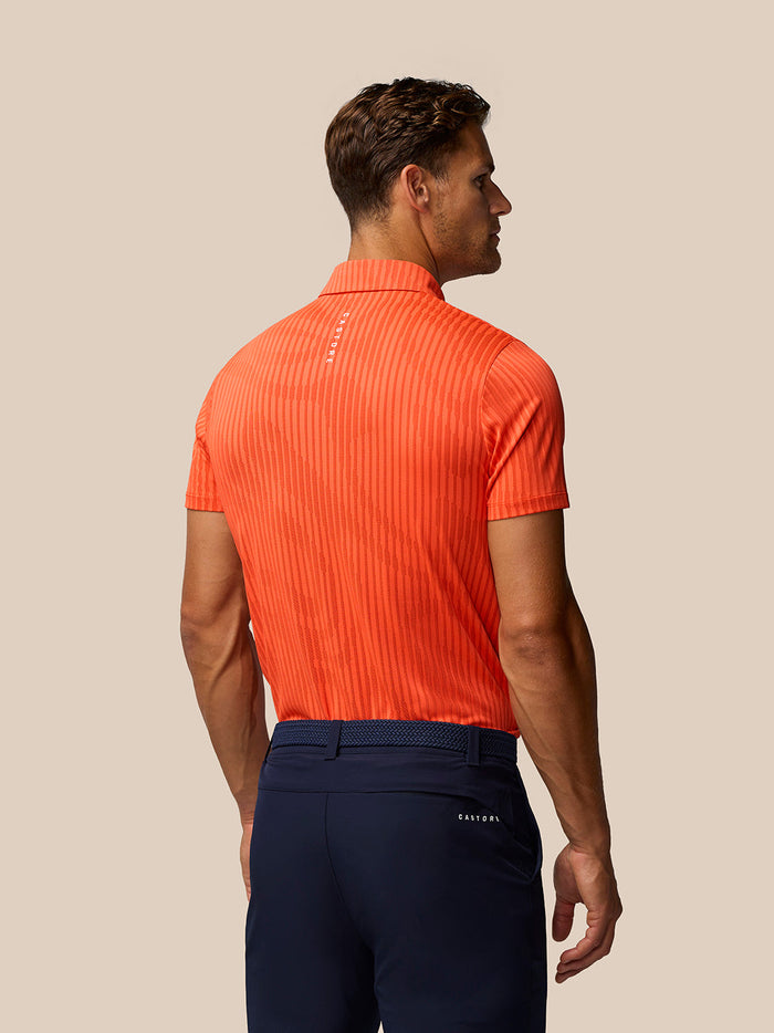 Back view of a man in a bright orange striped Golf Pinnacle Glow Polo.