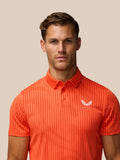 Close up of male model wearing bright orange striped golf polo with Castore logo on chest.