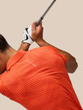 Golfer wearing Pinnacle Glow polo in bright orange with all over stripes and Castore logo on chest