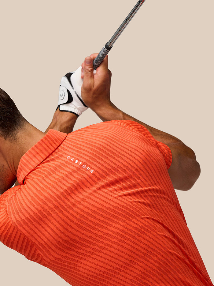 Golfer wearing Pinnacle Glow polo in bright orange with all over stripes and Castore logo on chest