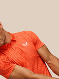 Partial view of bright orange striped golf polo showing Castore logo on chest and polo collar.