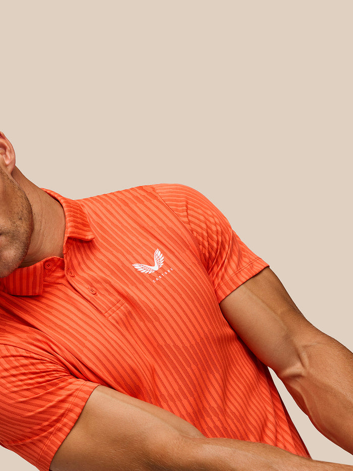 Partial view of bright orange striped golf polo showing Castore logo on chest and polo collar.