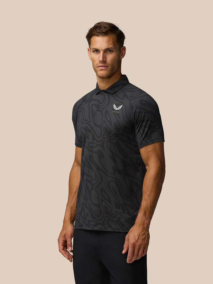 Front view of a man wearing a gunmetal grey golf polo with zebra pattern, three-button placket and Castore logo on the left chest.