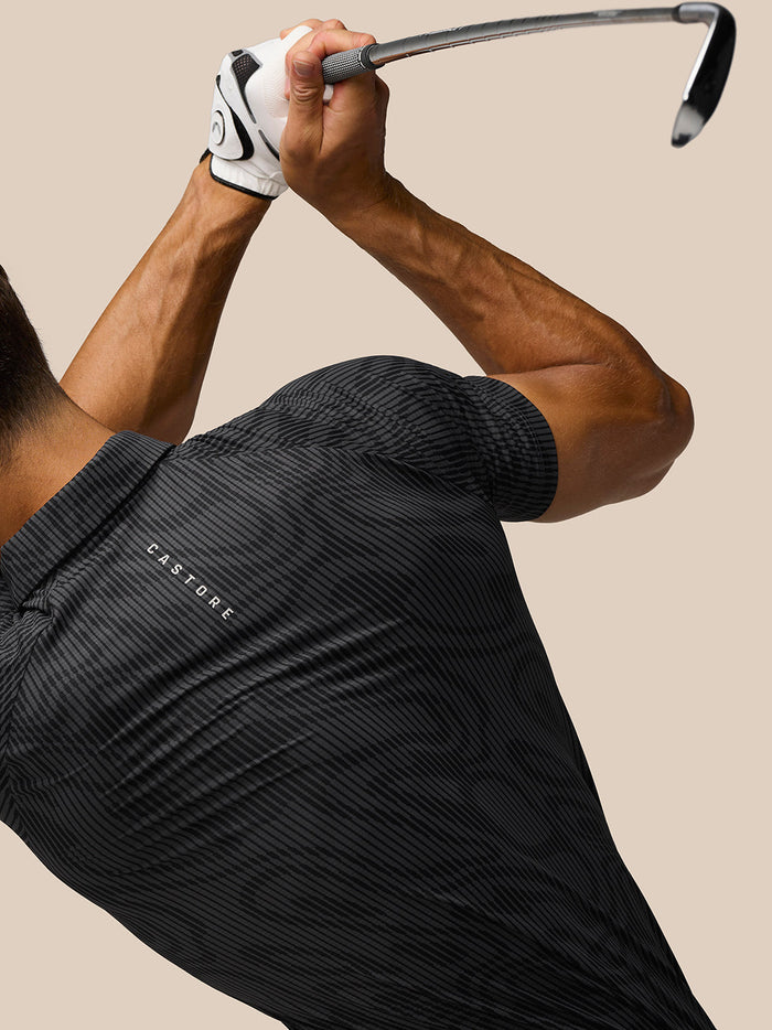 Athlete wearing Golf Club Glow Printed Polo with a dark striped pattern while swinging a golf club.